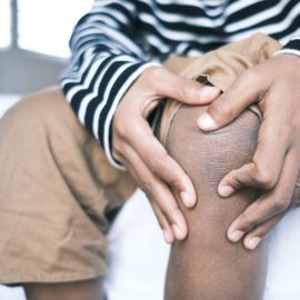 Man holding his knee due to knee pain while sitting at home